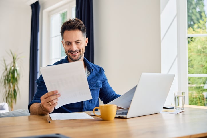man with financial paperwork on laptop