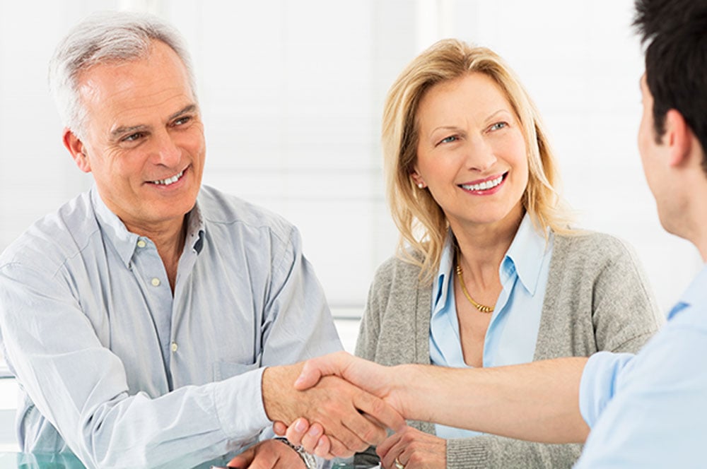 Older couple smiling and shaking hands with advisor